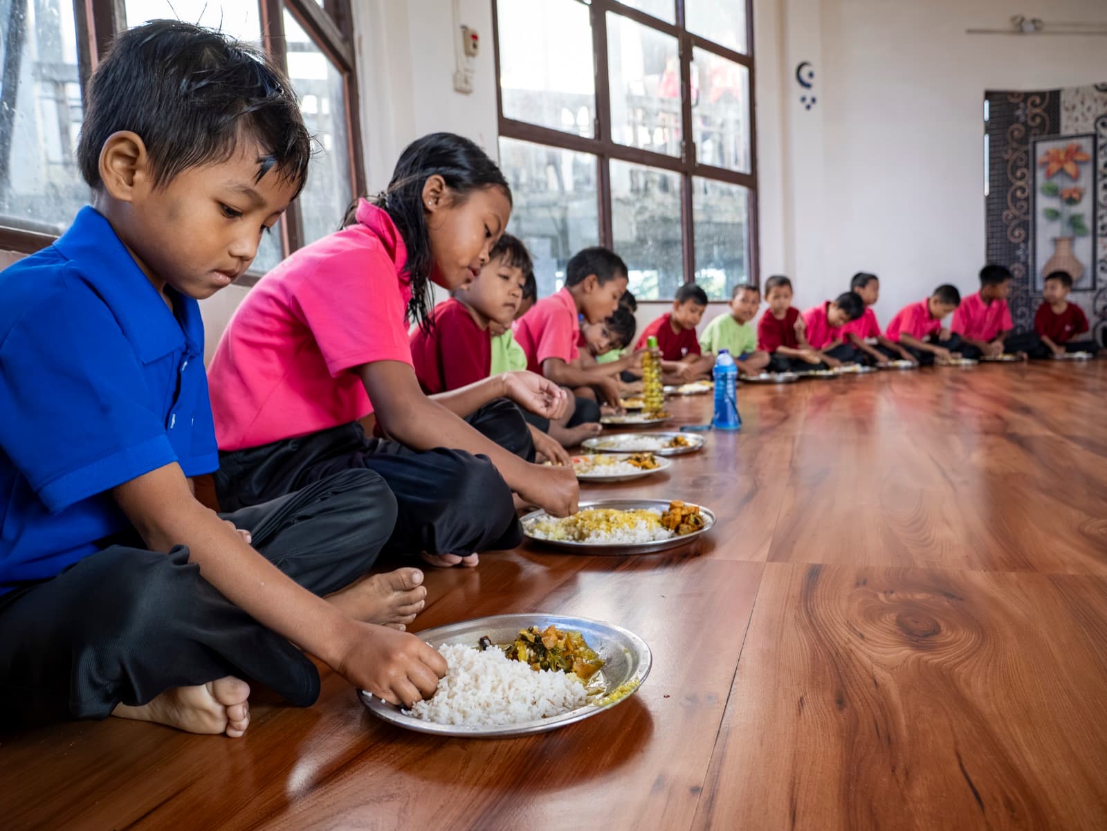 Children sharing a meal in the dining hall in window light